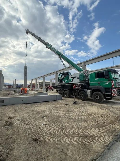 Macara mobilă și camioane la un șantier de viaduct din beton.