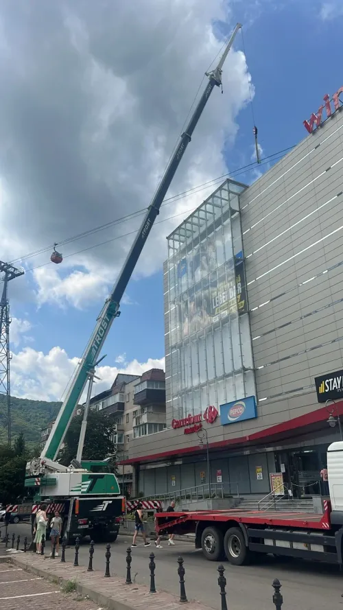 Automacara lucrând lângă fațada unui centru comercial din Piatra Neamț, cu telecabină vizibilă pe munte.