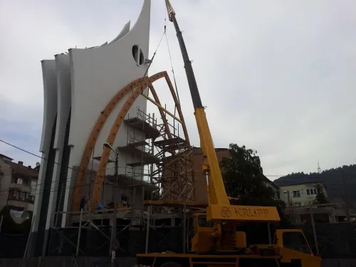 Macara mobilă montând un arc din lemn la o clădire cu arhitectură modernă.