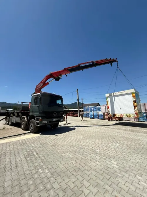 Macara pe camion ridicând un chioșc mobil, pregătit pentru amplasare.
