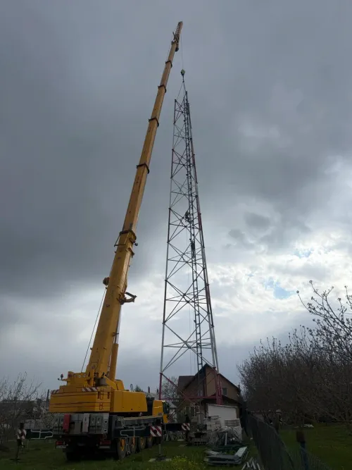 Automacara ridicând un stâlp pentru antenă de telecomunicații, în curte rurală.