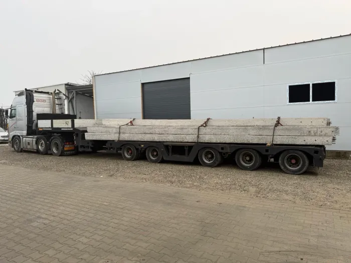 Cap tractor cu remorcă, pregătit pentru transportul unor grinzi de beton supradimensionate.