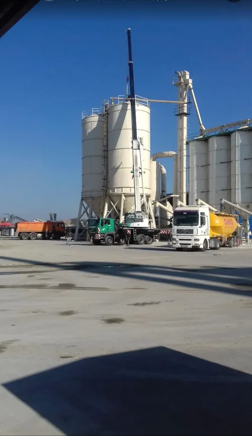 Automacara lucrând lângă silozurile unei fabrici de ciment.