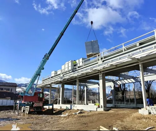 Automacara ridicând o încărcătură învelită, la structura metalică a unei clădiri, în zonă montană.