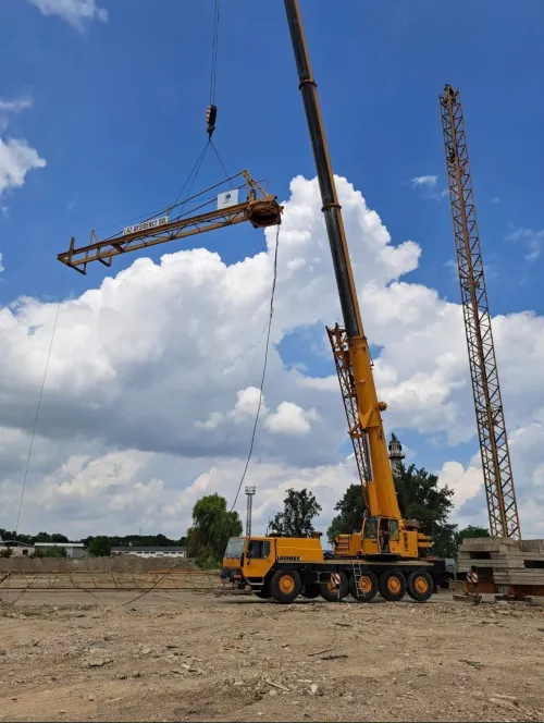Automacara ridicând o grindă metalică, la un șantier rezidențial, în zi de iarnă.