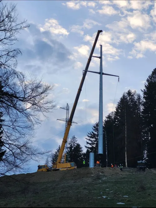 Automacara ridicând un stâlp de înaltă tensiune, în zonă împădurită montană.