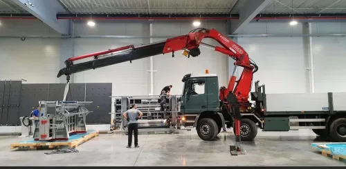 Macara pe camion manevrând o structură metalică într-o hală industrială.