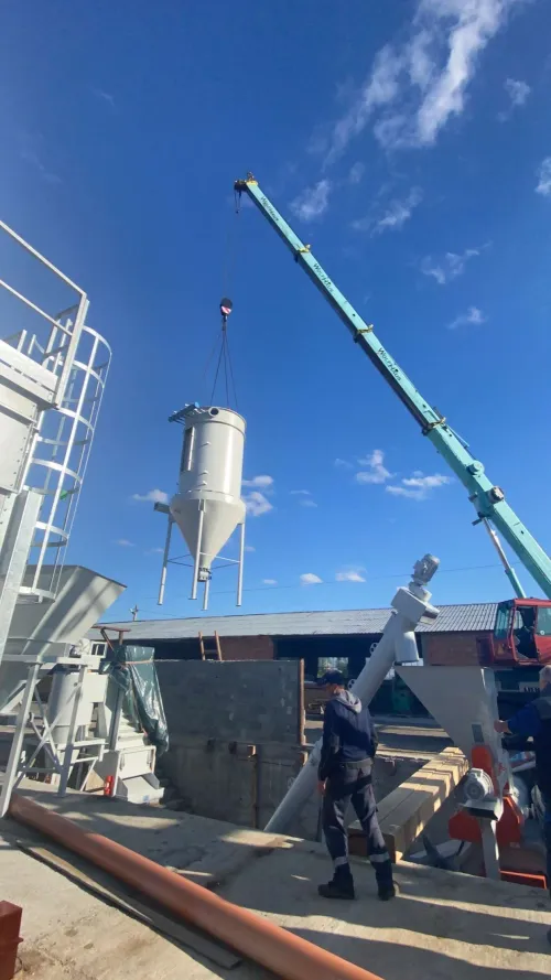 Automacara ridicând un siloz metalic cilindric, lângă acoperișul unei hale industriale.