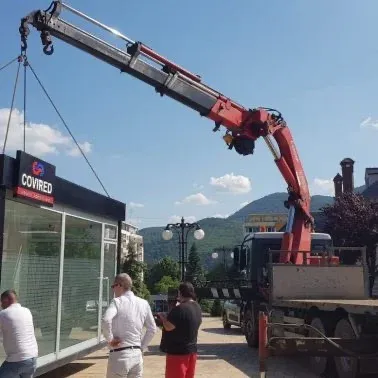 Macara pe camion ridicând materiale lângă un magazin, în centrul localității.