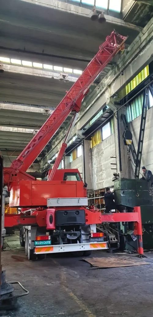 Automacara ridicând un utilaj industrial, într-o hală de producție.