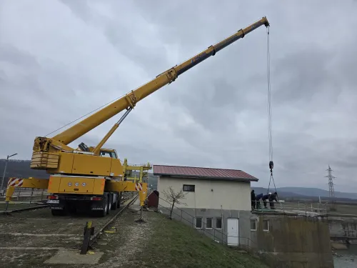 Automacara ridicând echipamente la o construcție hidrotehnică, în zonă montană.