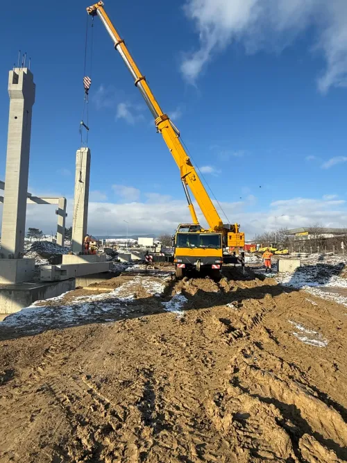 Automacara ridicând un pilon de beton, la un șantier de drum, iarna.