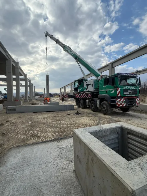 Automacara poziționând un stâlp de beton, la un șantier industrial.