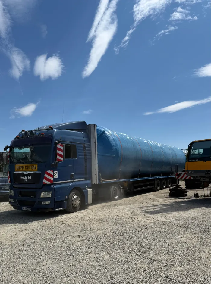 Transport agabaritic de rezervor cilindric albastru, prins cu chingi pe platformă cu trailer.